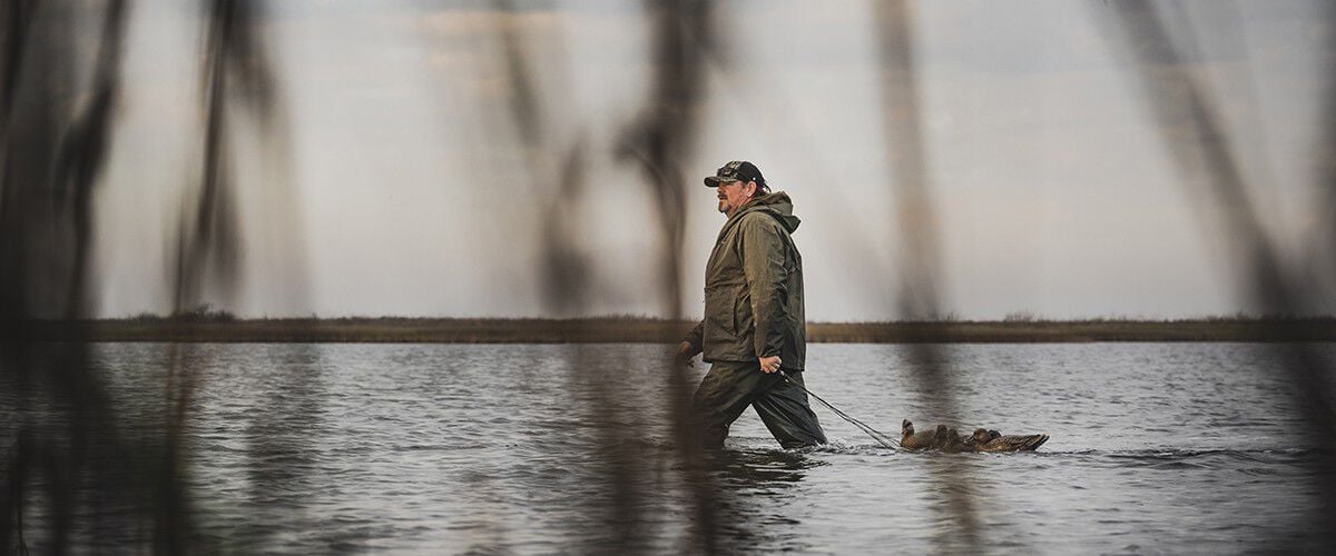 man walking through water with duck decoys